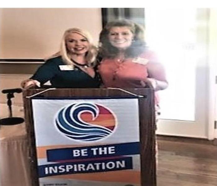 two women standing at a podium at a rotary meeting