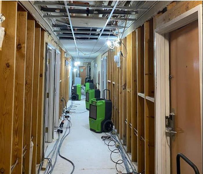 SERVPRO air dryers in a hallway with exposed 2X4 walls and a door